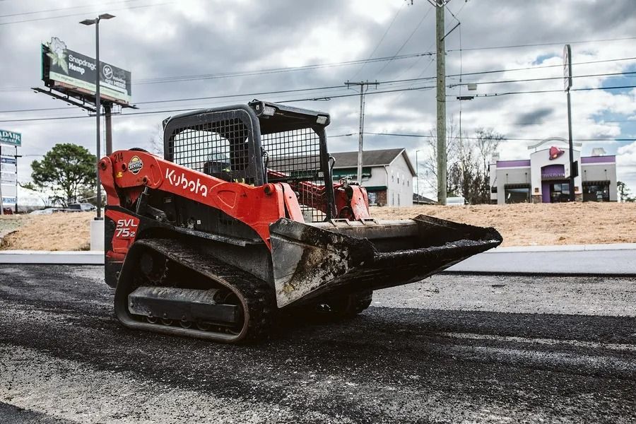 Red Kubota track loader on asphalt road with fast food restaurant in the background.