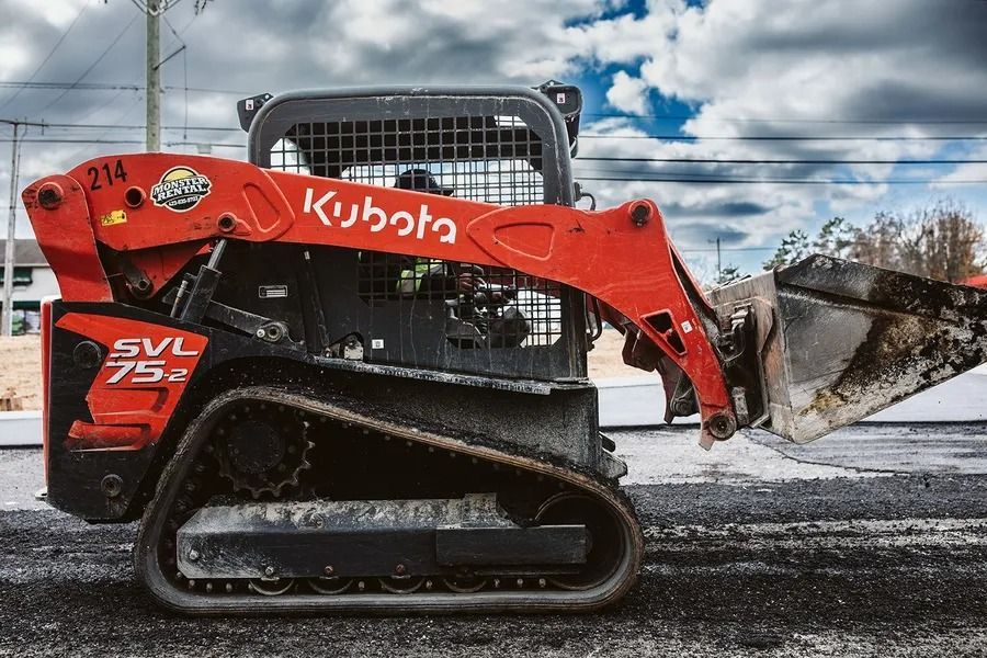 Red Kubota SVL 75-2 skid steer loader on tracks scooping asphalt on a road.