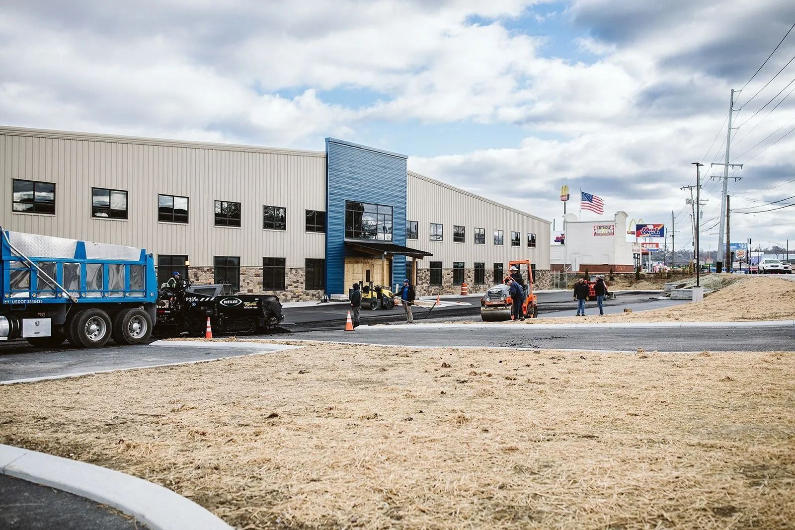 Construction site with building and vehicles; blue truck, sky, road, and workers.
