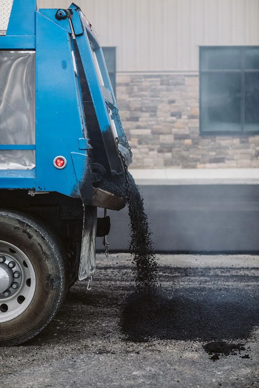 Blue dump truck unloading asphalt onto a paved road.