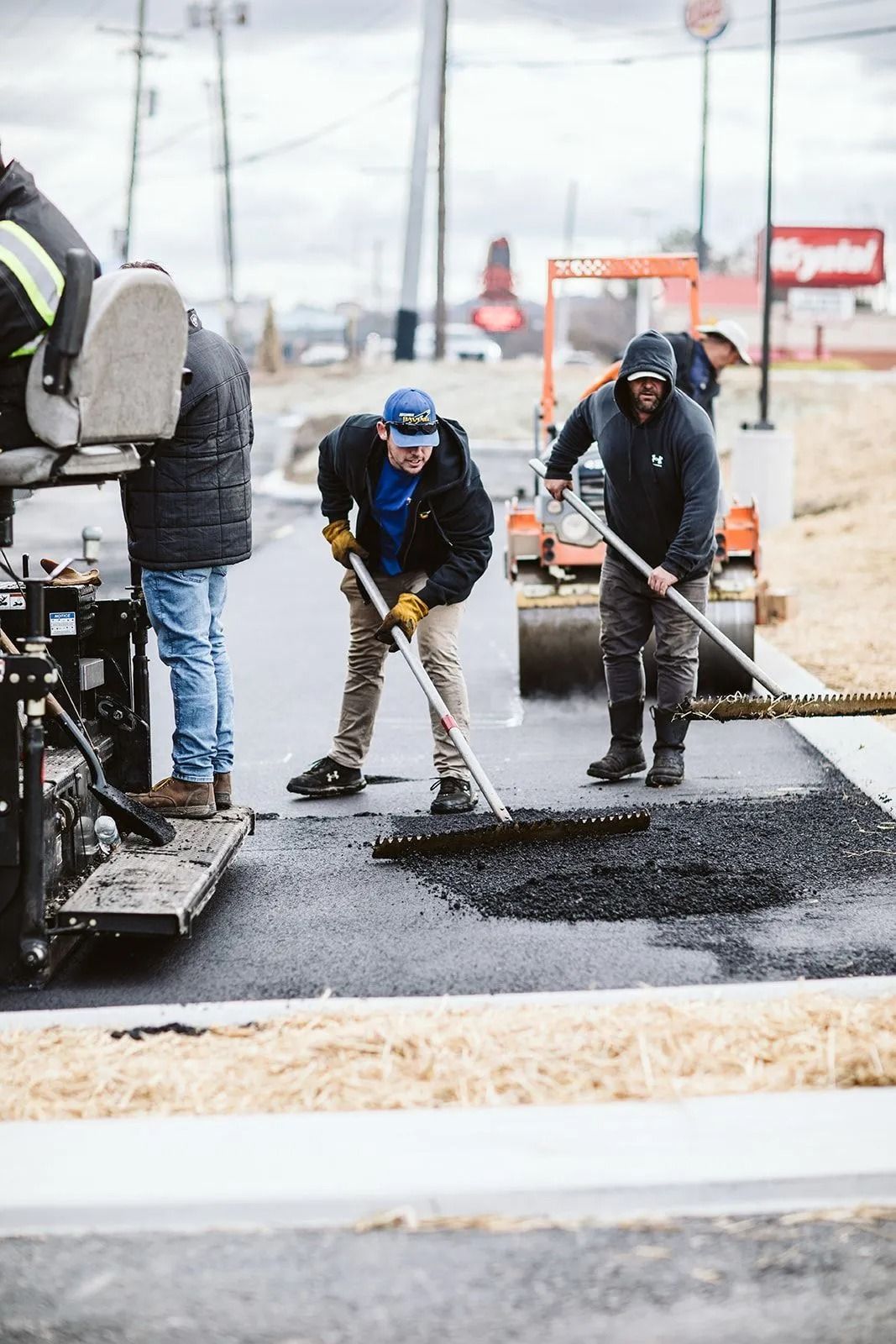 Road construction workers paving asphalt near a fast-food restaurant.