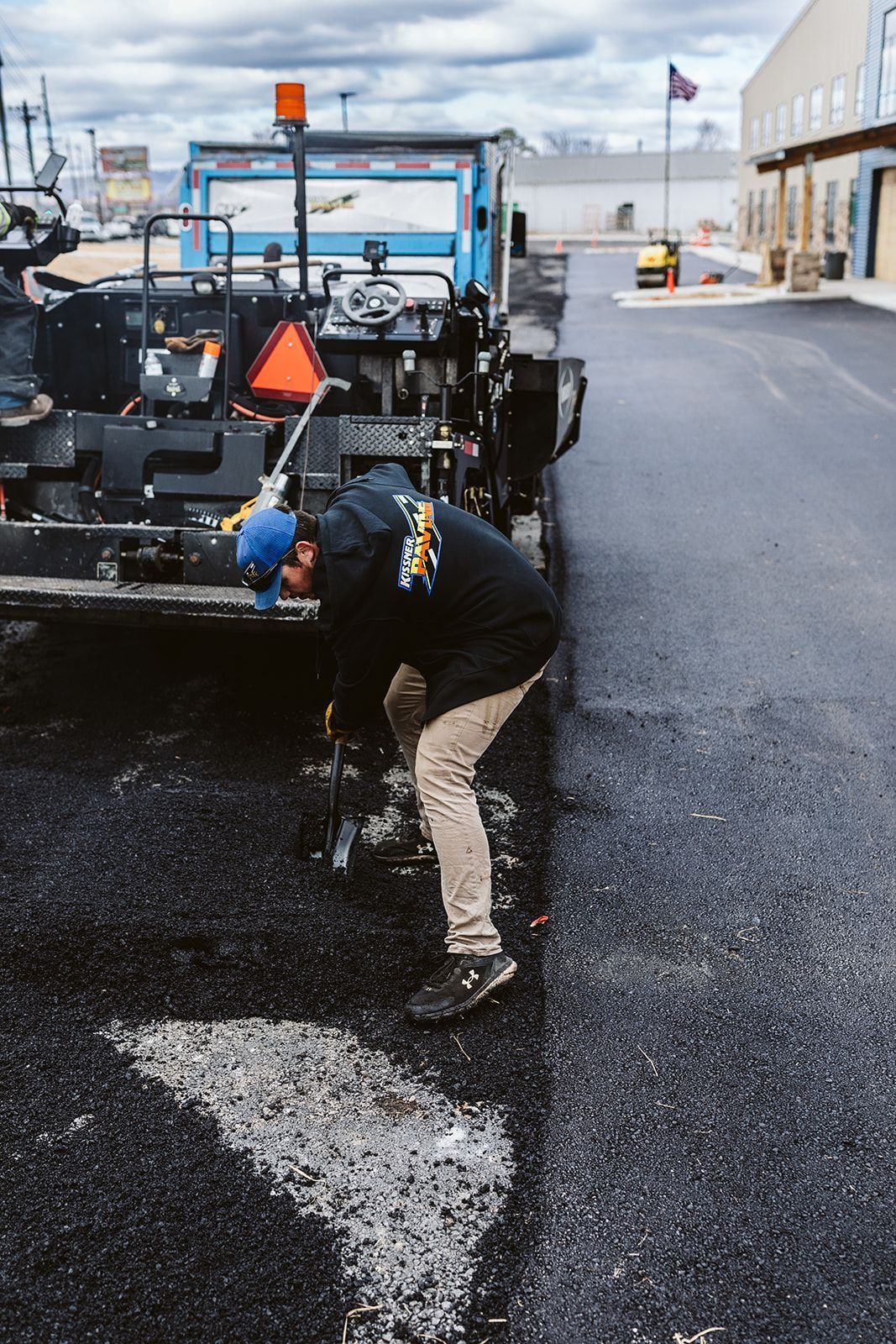 Man in blue hat working on asphalt with paving machine.