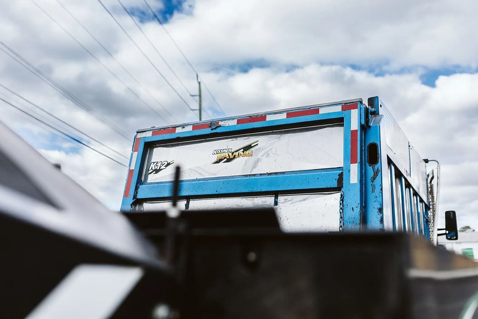 Blue and silver garbage truck with reflective stripes against a cloudy sky.
