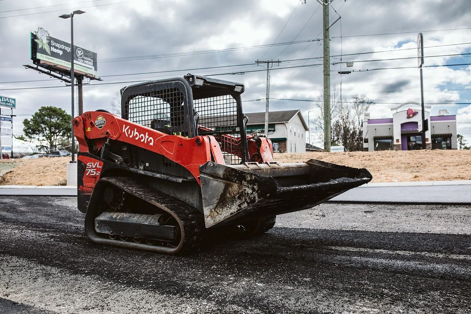 Red Kubota skid steer on asphalt with a Taco Bell in the background.