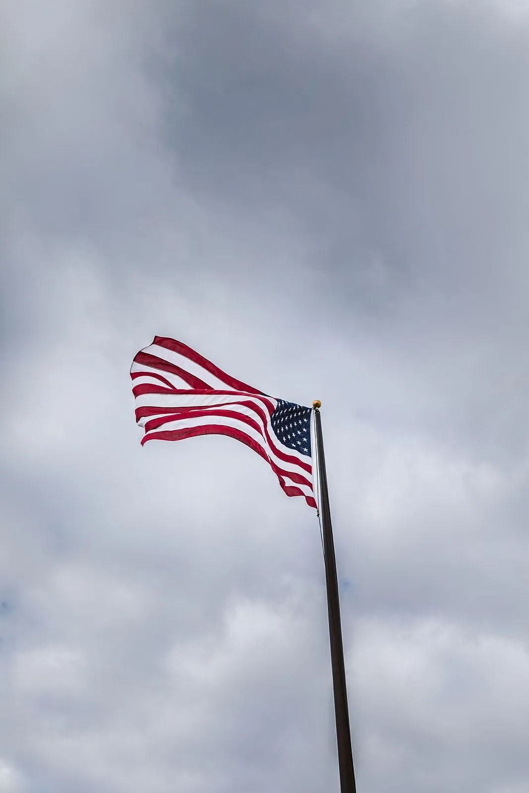 American flag waving on a pole against a cloudy sky.