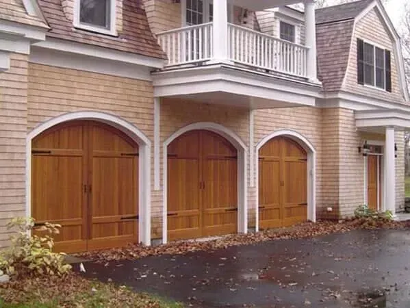 Three wooden garage doors on a tan townhouse exterior with white trim and a wet driveway