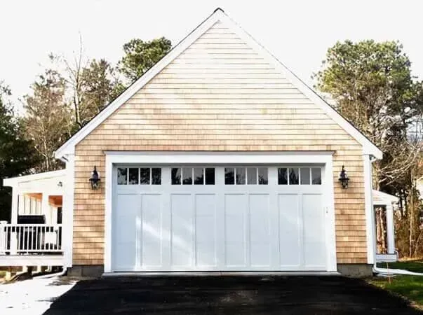 White garage door on a beige house with a peaked roof and snowy yard