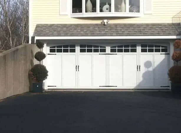 White garage doors on a beige house with a dark driveway and trimmed topiary on the left and right.