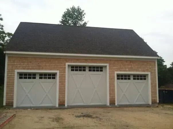 Three-car garage with white doors and a dark roof on a brick building, viewed from the front.