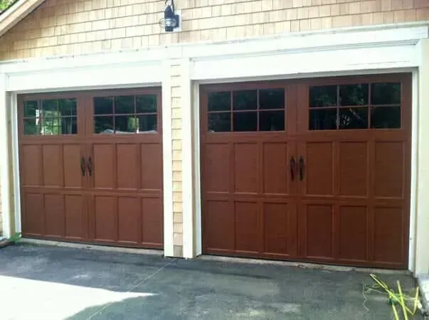Two brown wooden garage doors on a beige house exterior