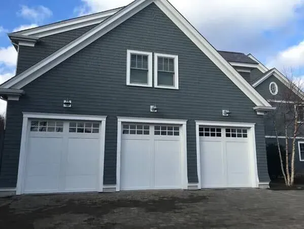 Gray house with three white garage doors and a small upper window under a cloudy sky