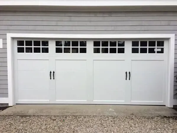 White four-car garage door with small window panes, set in a gray house exterior.