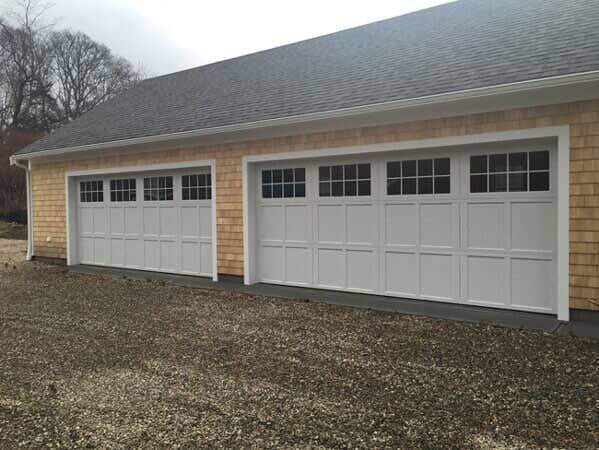 Two white garage doors on a brick house with a gray roof and gravel driveway