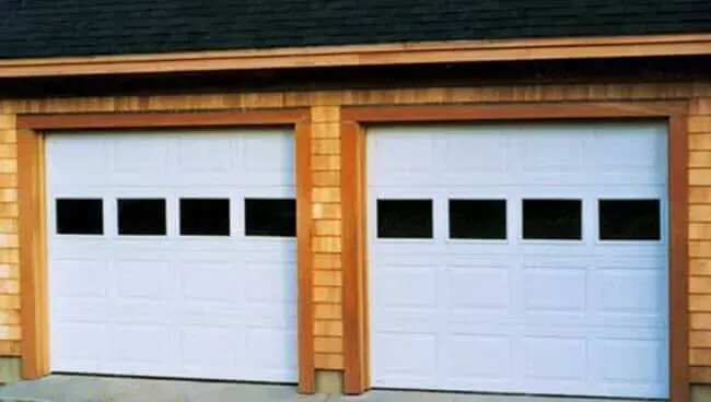 Two white garage doors with black windows on a brick house front