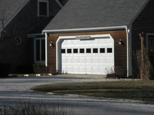 Suburban house with a white garage door beside a driveway and lawn at dusk
