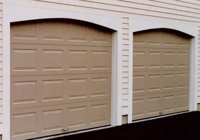 Two beige garage doors on a light-colored siding wall