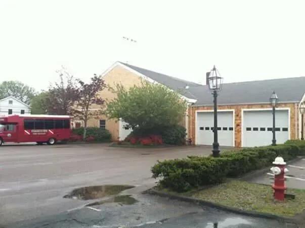 Wet suburban house with two garage doors, red van, lamp post, and fire hydrant under overcast sky