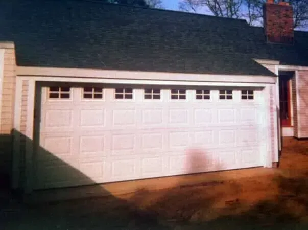 White double garage door on a house exterior, with a dark roof and brick chimney in sunlight.