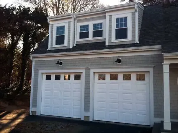 Two-car white garage with dormer windows and black trim on a house exterior