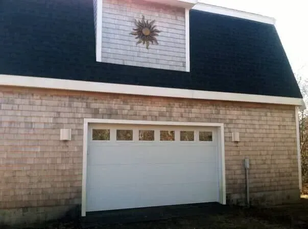 White garage with dark blue roof shingles and a sunburst decoration above the door.