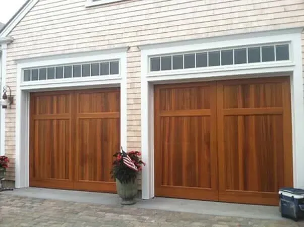 Two wooden garage doors with white trim on a light siding house exterior
