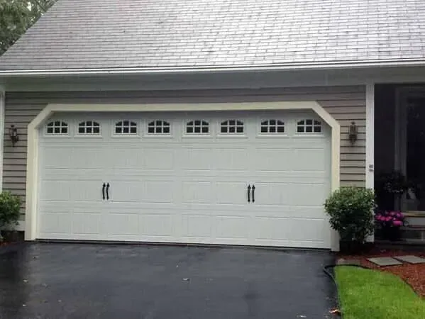 White double garage door with decorative windows on a suburban house, dark driveway in front