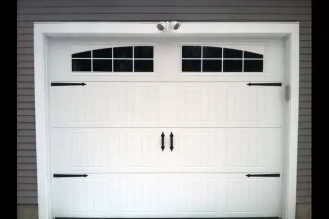 White garage door with small window panes and black handles on a gray house exterior