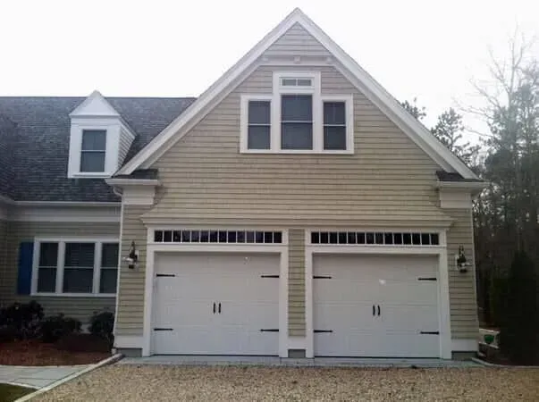 Suburban house with beige siding and a two-car white garage on a cloudy day