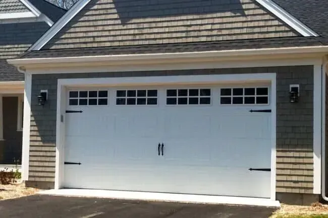 White double garage door on a house with gray siding and a shingled roof