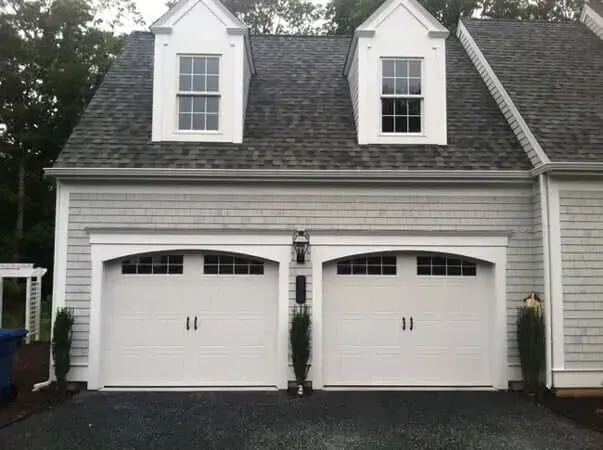 White two-car garage with dormer windows and gray siding on a house façade