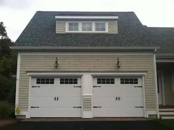 Two-car beige garage with white doors and a dormer window above