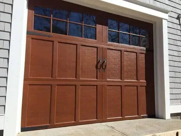 Brown paneled garage door with small upper windows and black handles under white trim