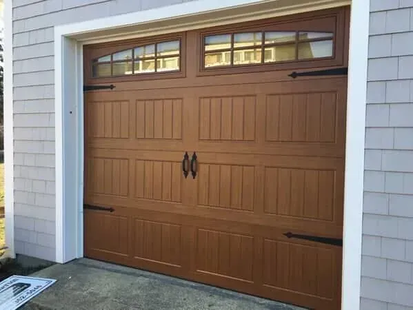 Brown garage door with small upper windows in a light gray house exterior