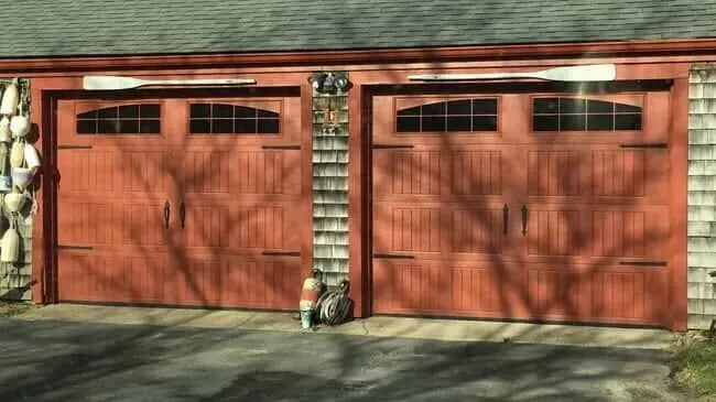 Two red double garage doors on a brick house, with stone columns and a sunlit driveway