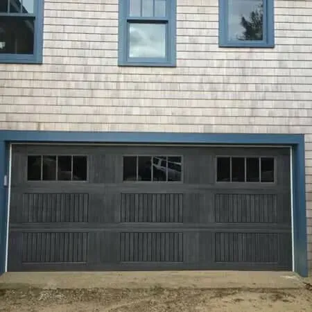 Dark gray double garage door with small windows beneath a gray-shingled house exterior