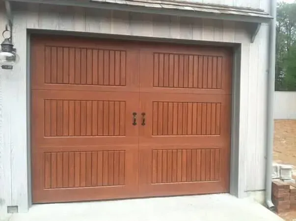 Wooden double garage door with vertical slats and handles set in a white concrete frame