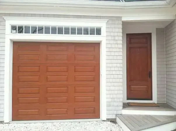 Front view of a house with a large brown garage door and a matching front entry door on a white facade.
