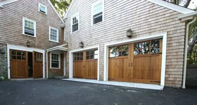 Two-car wooden garage doors on a gray shingled house with a black asphalt driveway