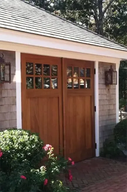 Wooden double garden doors with small windows on a cottage exterior, framed by white trim and flowers