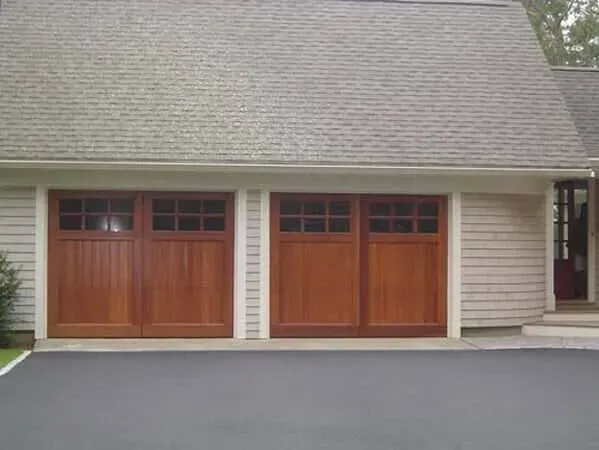 Two wooden garage doors on a beige house with gray shingle roof
