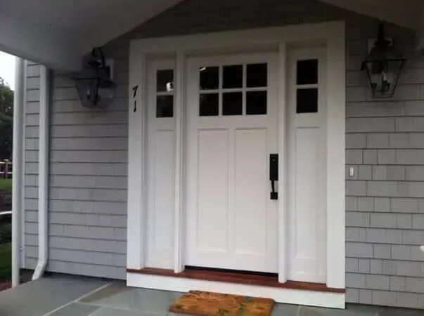 Front porch entrance with a white door, sidelights, gray siding, and wall lanterns