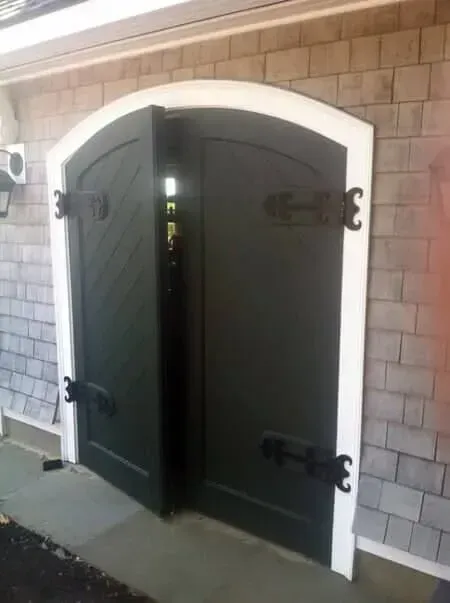 Arched black double doors with white trim set in a stone building wall.
