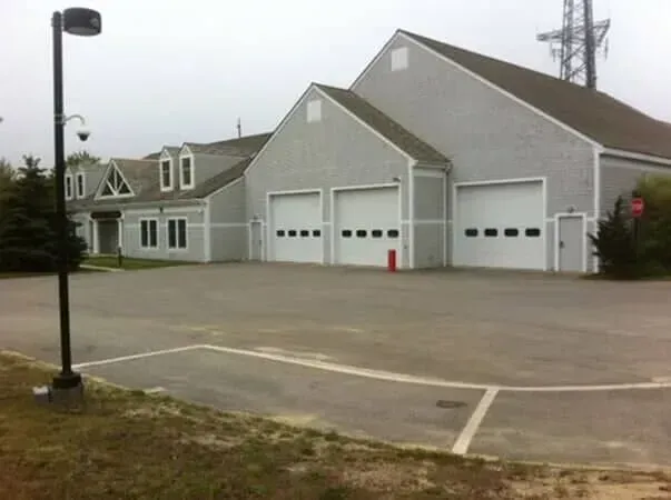 Gray fire station with three garage bays and a parking lot in front
