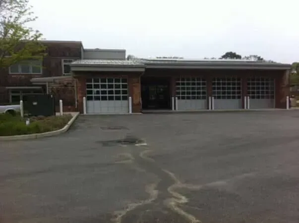 Brick fire station with three garage doors and a wide empty asphalt lot in front