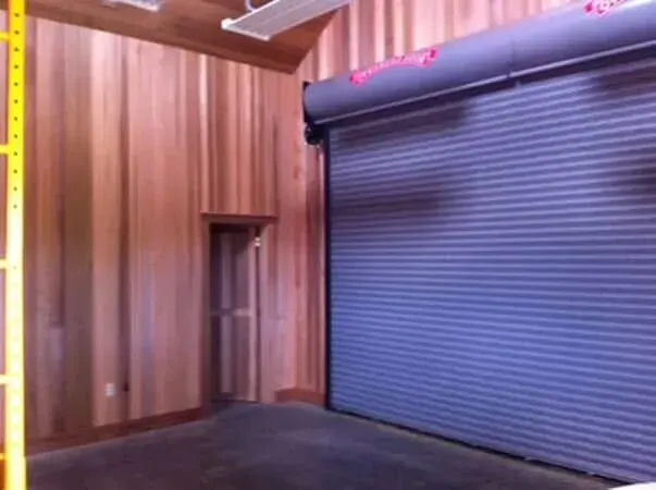 Wood-paneled interior with a dark roll-up garage door and black floor mat.