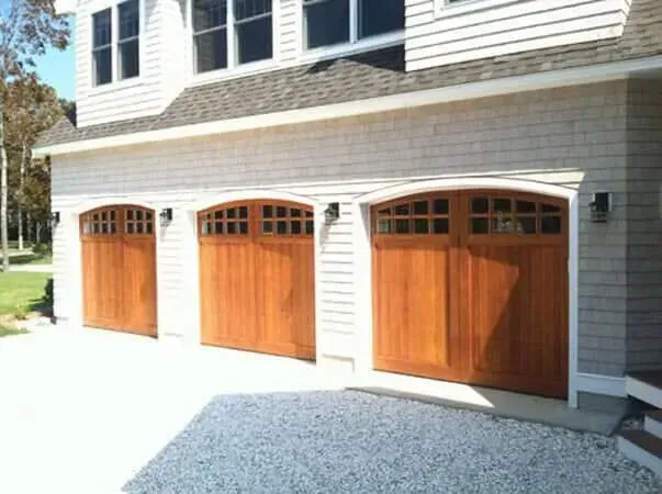 Three wooden garage doors with arched windows on a gray house exterior