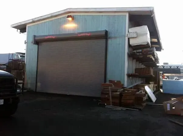 Industrial warehouse with a closed roll-up door and stacked materials outside on a cloudy day