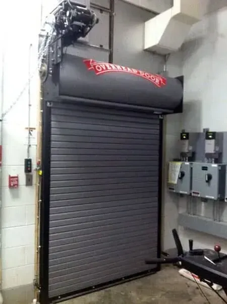 Closed gray metal roll-up door in an industrial room with wall-mounted electrical panels