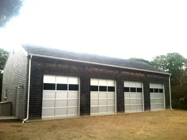 Three-car garage with white doors and dark siding on a grassy lot