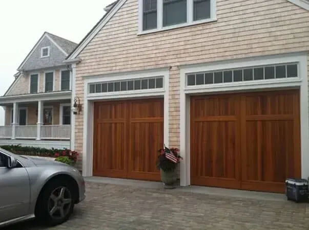 Suburban house with two wooden garage doors, shingled siding, and a car parked in the driveway.